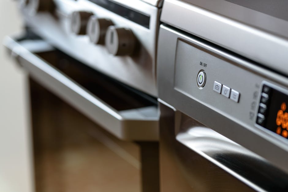 Close-up image of a modern stainless steel oven with a digital control panel and a large glass door, showcasing a clean and polished surface. The oven is situated in a contemporary kitchen with wooden flooring and minimalistic cabinetry. The control knobs above the oven are neatly aligned, and the area appears well-maintained, reflecting an emphasis on hygiene and surface cleanliness, consistent with deep cleaning and sanitisation services provided by Oven Cleaning Ilford for residential or commercial spaces. The image highlights the sleek surface and advanced features designed for efficient domestic cleaning and upkeep.